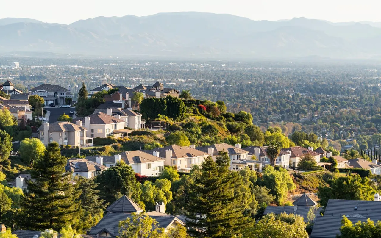 Aerial view of a luxury hillside community in Southern California with large homes, green trees, and distant mountains.