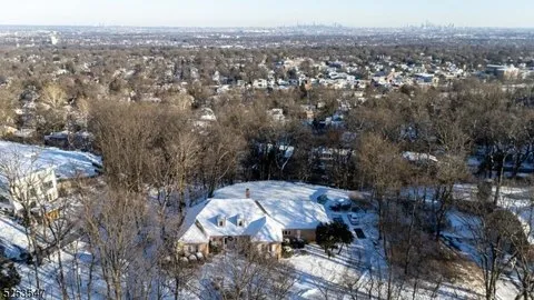 Aerial view of a luxury home with a snow-covered roof in a wooded Southern California neighborhood.