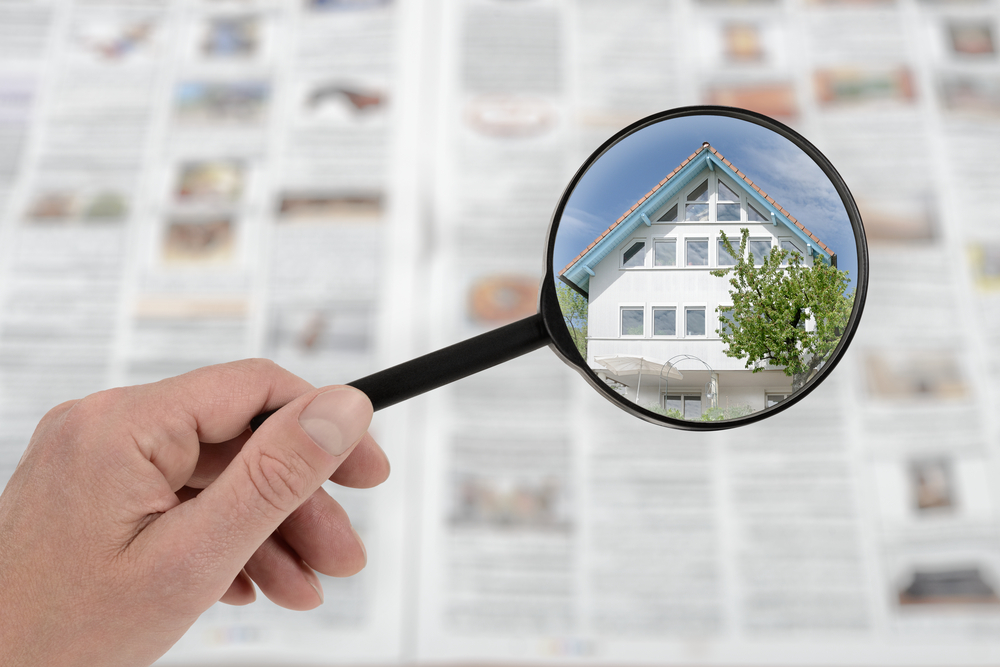 A magnifying glass focusing on a luxury home listing in a Southern California real estate newspaper.