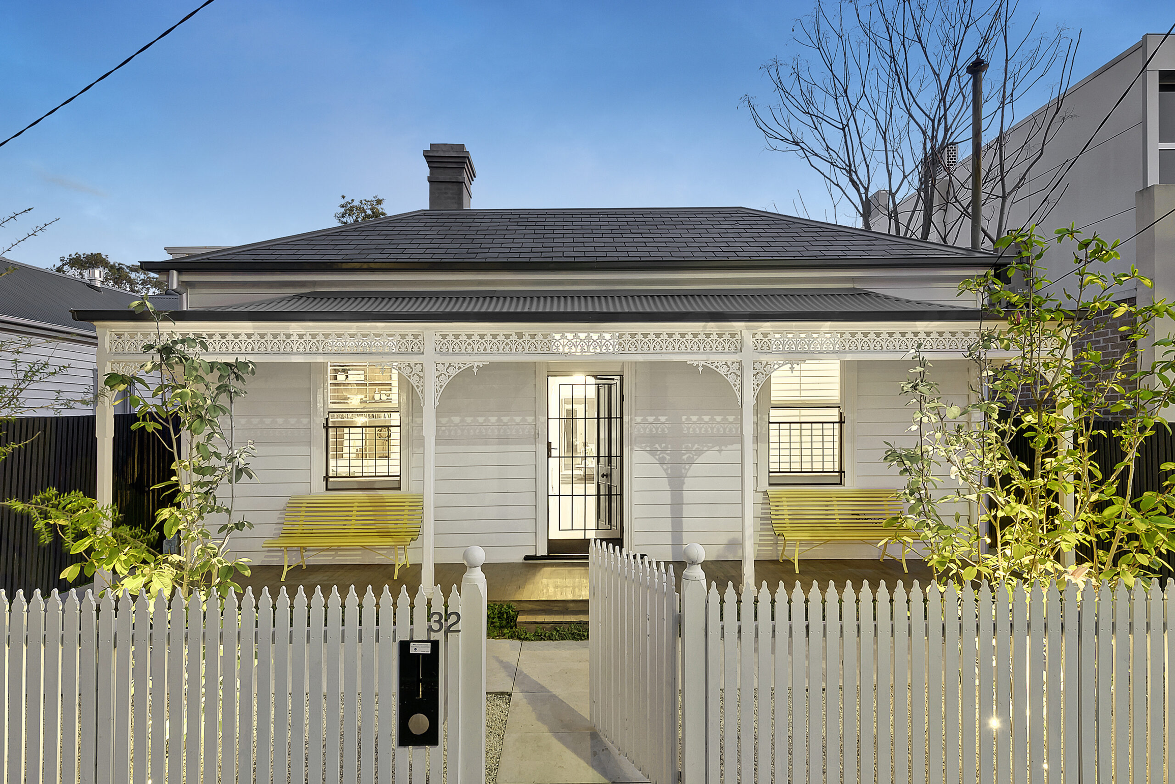 Victorian-style cottage in Southern California with a white fence, decorative trim, and a front porch with yellow benches.