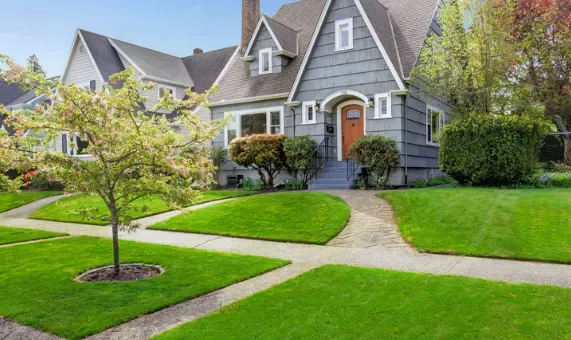 Exterior of a grey Tudor-style luxury home in Southern California with gabled roofs, green lawn, and a stone walkway.