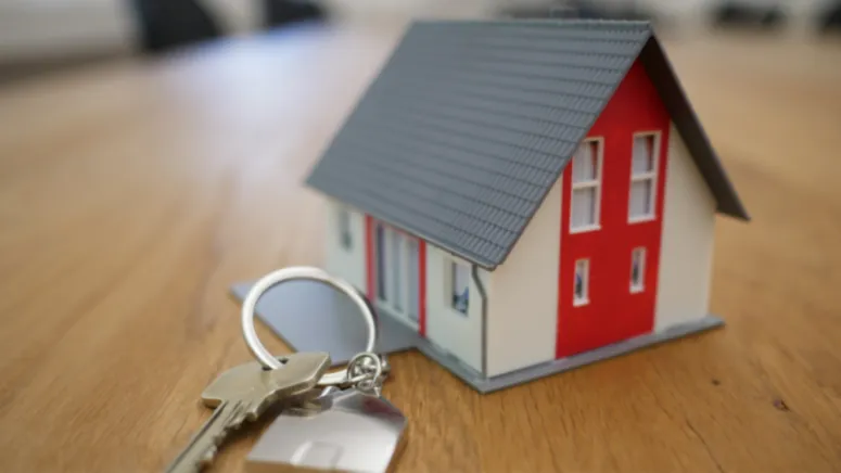Close-up of house keys on a wooden table next to a small model home, representing Southern California homeownership.