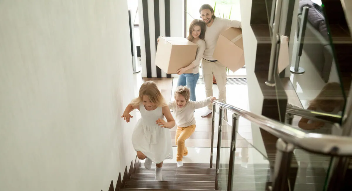 A family on the staircase with two kids playing and a happy parent holding boxes.