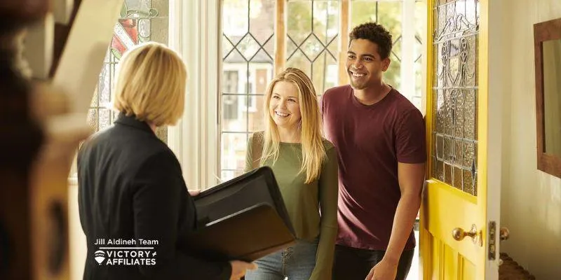 Real estate agent from the Jill Aldine Team welcoming a young couple to a luxury Southern California home with a yellow door.