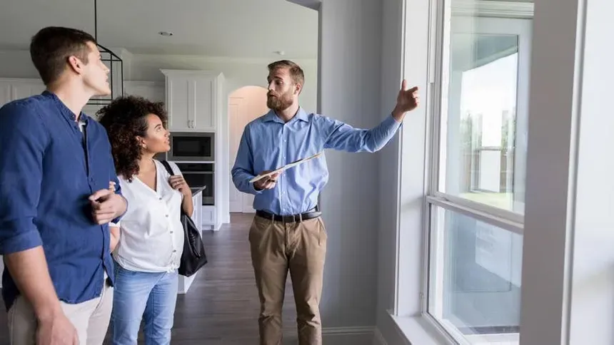 Real estate agent showing a modern luxury home interior to a young couple in Southern California.