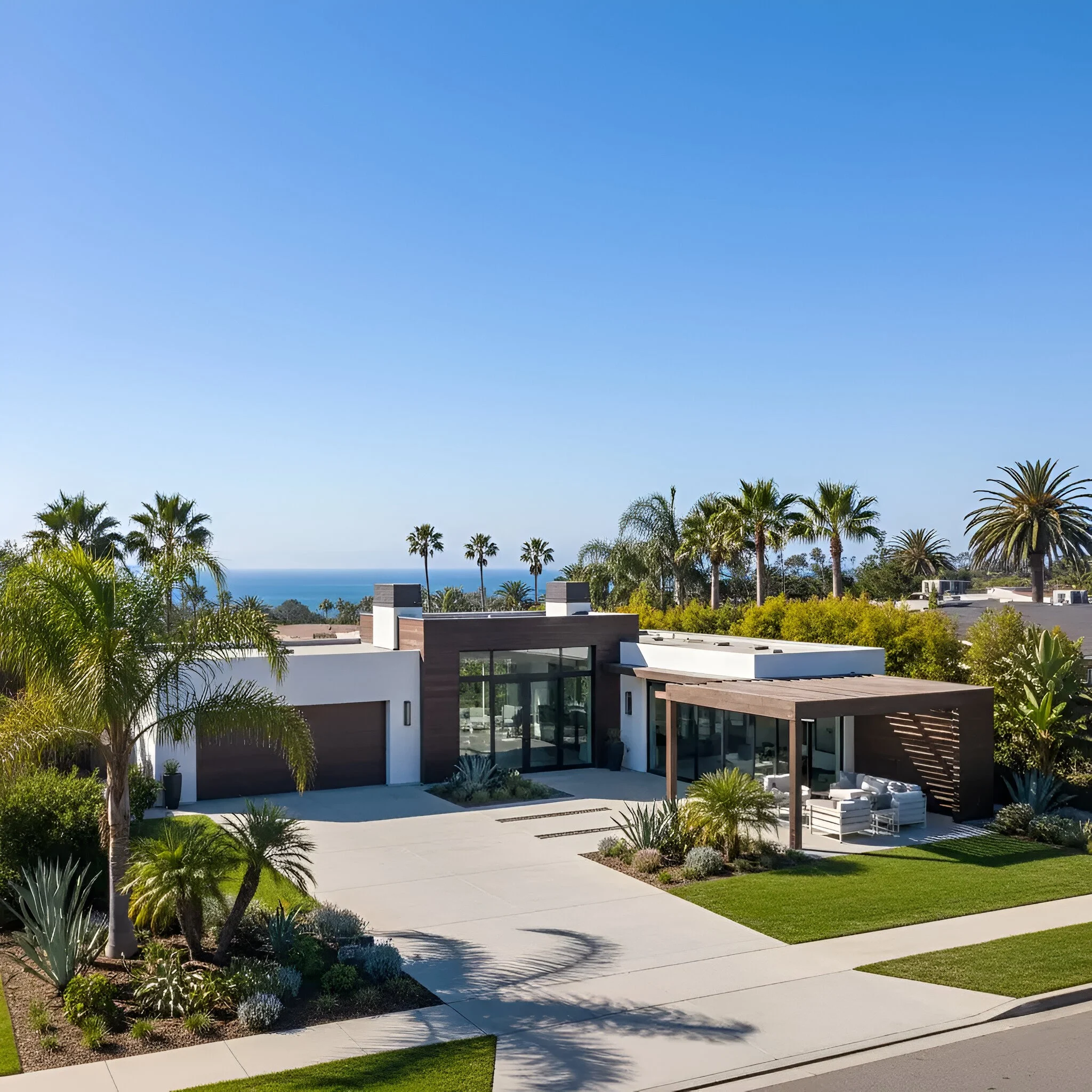Sunlit exterior of a modern Southern California villa with white stucco, dark wood siding, flat roof, and outdoor lounge with ocean views.